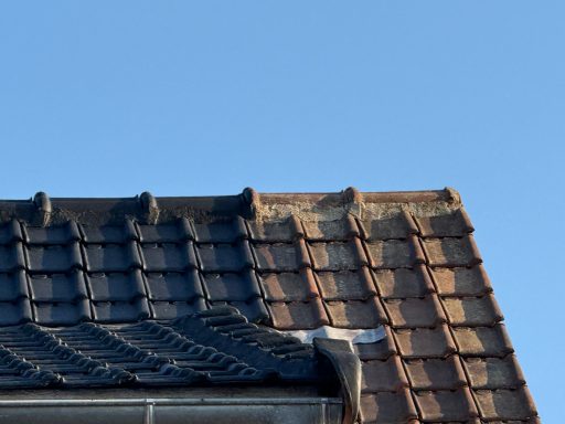 Toit en tuiles avec différentes teintes sous un ciel bleu clair.