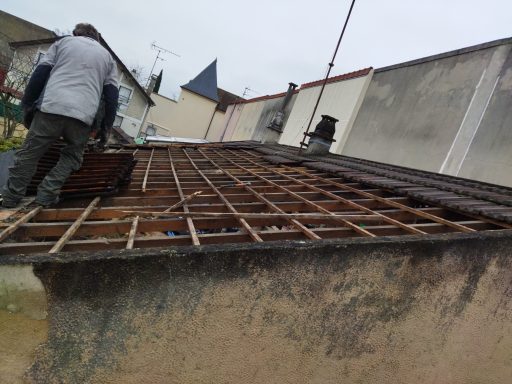 Un ouvrier travaille sur une charpente en bois d'un toit en rénovation.